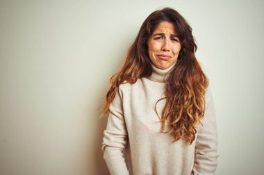 Genç güzel kadın beyaz izole arka plan üzerinde ayakta kış kazak giyen depresif ve sıkıntı için endişe, kızgın ve korkmuş ağlıyor. Hüzünlü ifade.