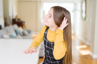 Güzel genç kız çocuk bir işitme söylenti ya da dedikodu için dinleme kulak üzerinde el ile gülümseyen masada oturuyor. Sağırlık kavramı.