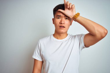 İzole beyaz arka plan üzerinde duran t-shirt giyen genç Asyalı Çinli adam alaycı ve aşağılayıcı kaybeden jest yapıyor alnına parmakları ile insanların alay yapma.