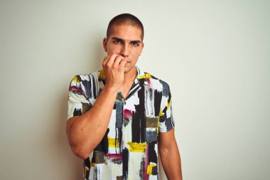 Beyaz izole arka plan üzerinde yazlık gömlek giyen genç yakışıklı adam stresli ve ağız tırnak ısırma elleri ile sinirli görünümlü. Anksiyete sorunu.