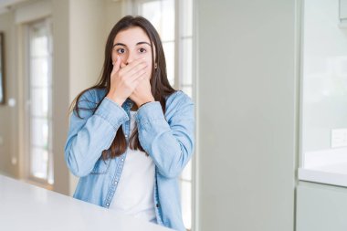 Evde beyaz masada oturan güzel genç kadın hata için elleri ile ağız kapsayan şok. Gizli kavram.