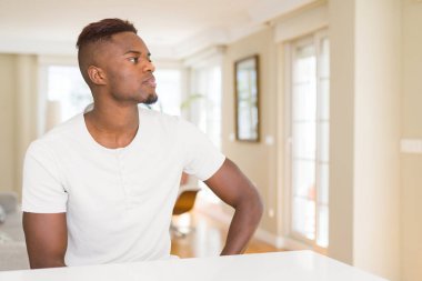 Yakışıklı afro-amerikan adam evde beyaz masada yan bakıyor, kendine güvenen gülümseme ile doğal yüzü ile profil poz dinlenmek.
