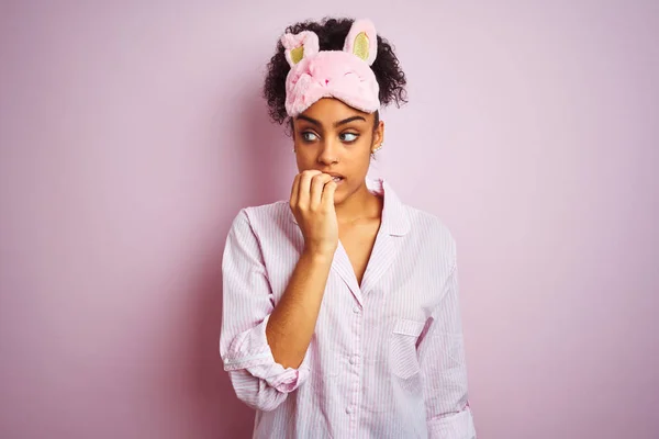 年轻的非洲裔美国妇女穿着睡衣和面具在孤立的粉红色背景看起来紧张和紧张与手咬指甲 焦虑问题 — 图库照片