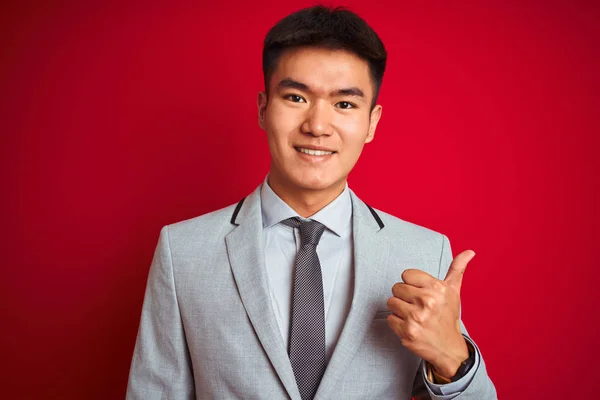亚洲华商身着灰色夹克 打着领带站在孤立的红色背景上 用手竖起欢快的大拇指 批准表达式 以显示成功的相机 — 图库照片