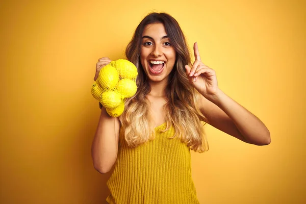 Mladá Krásná Žena Která Drží Síť Citronů Přes Žlutý Izolovaný — Stock fotografie