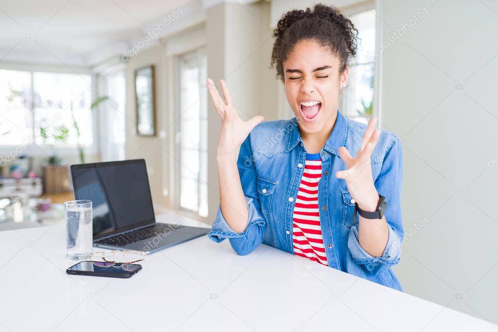 Young african american business woman working using computer laptop celebrating mad and crazy for success with arms raised and closed eyes screaming excited. Winner concept