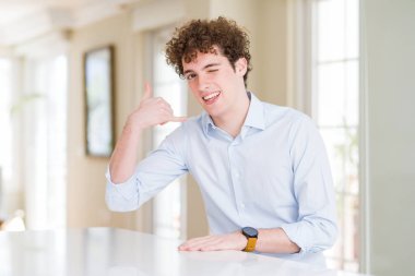 Kıvırcık okuyan genç iş adamı telefonda konuşmak gibi el ve parmaklarıyla telefon hareketi yaparak gülümseyerek başını okuyor. İletişim kavramları.