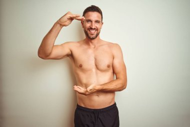 Büyük ve büyük boy işareti gösteren elleri ile izole arka plan gesturing üzerinde Genç yakışıklı gömleksiz adam, ölçü sembolü. Kameraya bakarak gülümsüyor. Ölçme kavramı.
