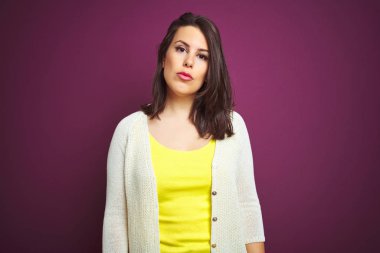 Genç güzel esmer kadın yüzünde ciddi ifade ile mor izole arka plan üzerinde bir ceket. Kameraya basit ve doğal bir bakış.