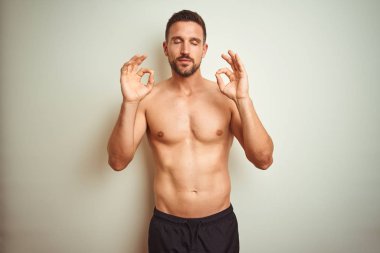 Izole arka plan üzerinde Genç yakışıklı gömleksiz adam dinlenmek ve gözleri parmakları ile meditasyon jest yapıyor kapalı gülümseyerek. Yoga konsepti.