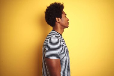 Afro saçlı Afro-Amerikan adam izole sarı arka plan üzerinde lacivert çizgili t-shirt giyen yan bakıyor, kendine güvenen gülümseme ile doğal yüzü ile profil poz dinlenmek.
