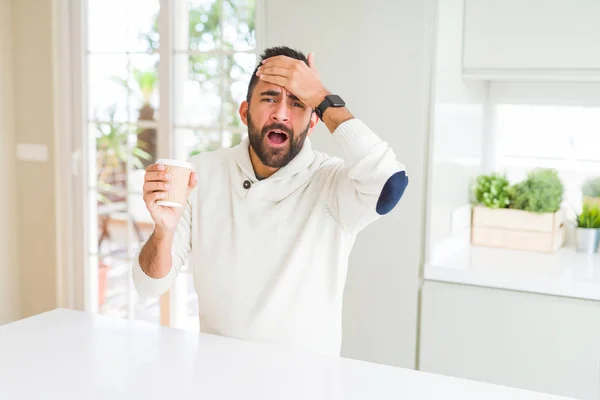 Handsome hispanic man drinking a coffee in a paper cup stressed with hand on head, shocked with shame and surprise face, angry and frustrated. Fear and upset for mistake.