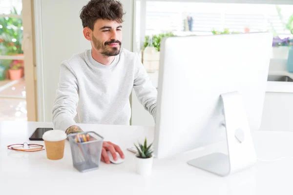 Fiatal jóképű ember dolgozik a számítógép segítségével, mosolyogva koncentrált — Stock Fotó