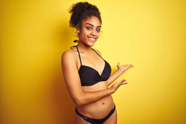 African american woman on vacation wearing bikini standing over isolated yellow background Inviting to enter smiling natural with open hand