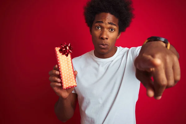年轻的非洲裔美国男子拿着情人节礼物站在孤立的红色背景 用手指指着相机和你 手签名 积极和自信的姿态从前面 — 图库照片