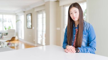 Uzun saçlı genç güzel Asyalı kadın kot ceket giyiyor yüzünde ciddi ifade ile rahat. Kameraya basit ve doğal bir bakış.