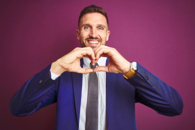 Mor izole arka plan üzerinde genç yakışıklı iş adamı aşk kalp sembolü ve elleriyle şekil gösteren gülümseyerek. Romantik kavram.