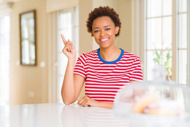 Kameraya bakarak yan el ve parmak ile işaret eden genç güzel Afrikalı-Amerikalı kadın evde yüzünde kocaman bir gülümseme ile.