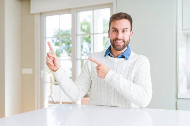 Rahat kazak giyen yakışıklı adam gülümseyerek ve yan iki el ve parmakları ile işaret kamera bakıyor.