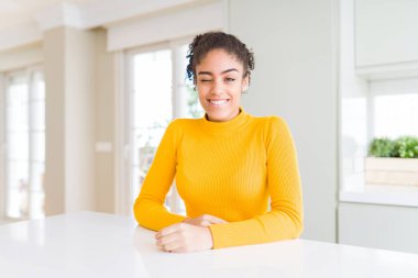 Seksi ifade, neşeli ve mutlu yüz ile kameraya bakarak rahat bir sarı kazak göz kırpma giyen afro saçlı güzel afro-amerikan kadın.