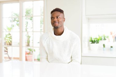 Yakışıklı afro-amerikan adam beyaz masada gülümseyerek yan bakıyor ve düşünme uzak bakıyor.