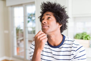 Afrikalı Amerikan adam çizgili t-shirt ile el çene üzerinde soru hakkında düşünme, dalgın ifade giyiyor. Düşünceli bir yüz ile gülümsüyor. Şüphe kavramı.