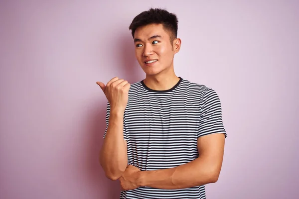 孤立したピンクの背景の上に立つストライプのTシャツを着た若いアジア人の男性は 幸せそうな顔で微笑み 親指を上げて横を向いている — ストック写真