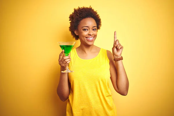 Young african american woman with afro hair drinking a cocktail over yellow isolated background surprised with an idea or question pointing finger with happy face, number one
