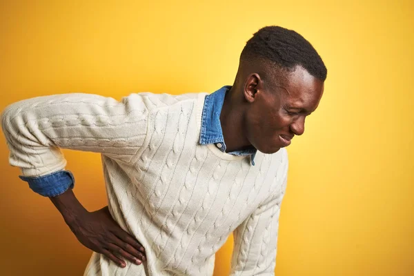 孤立した黄色の背景の上にデニムシャツと白いセーターを着たアフリカ系アメリカ人男性が腰痛の苦しみ 手で触れ 筋肉痛 — ストック写真