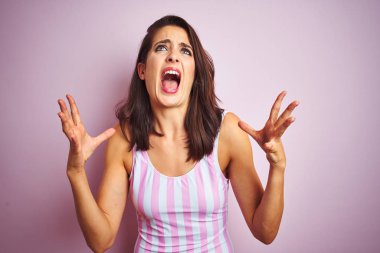Genç güzel kadın pembe izole arka plan deli ve deli bağırarak üzerinde çizgili pembe mayo mayo giyen ve agresif ifade ve kollar kaldırdı ile bağırıyor. Hayal kırıklığı kavramı.