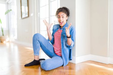 Afro saç ile güzel genç Afrikalı Amerikan kadın yerde oturan çılgın kutluyor ve başarı için hayran silah ile yükseltilmiş ve açık gözleri heyecanlı çığlık. Kazanan kavramı