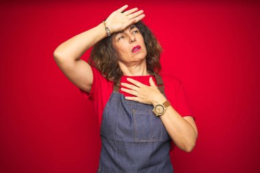 Kırmızı izole arka plan üzerinde önlük üniforma giyen orta yaş yaşlı kadın hastalık ve ateş, grip ve soğuk algınlığı, virüs hasta için alın dokunmadan