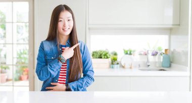 Yüze mutlu ve doğal ifade ile yan kadar el ve parmak ile işaret yüz bir gülümseme ile beyaz masa neşeli üzerinde denim ceket giyen güzel Asyalı kadın