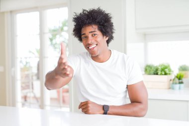 Genç afro-Amerikan adam rahat beyaz t-shirt giyen evde gülümseyerek selamlama ve karşılama olarak el sıkışma sunan dostu gülümseyerek. Başarılı iş.