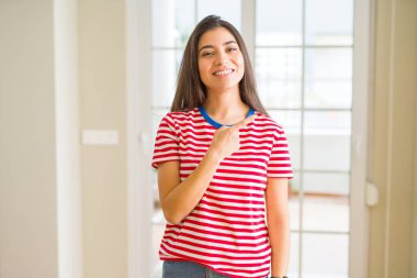 Rahat t-shirt neşeli bir gülümseme ile el ve parmak kadar yan yüzünde mutlu ve doğal ifade ile işaret yüz giyen genç güzel kadın