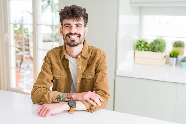 Young man wearing casual jacket sitting on white table with a happy and cool smile on face. Lucky person.