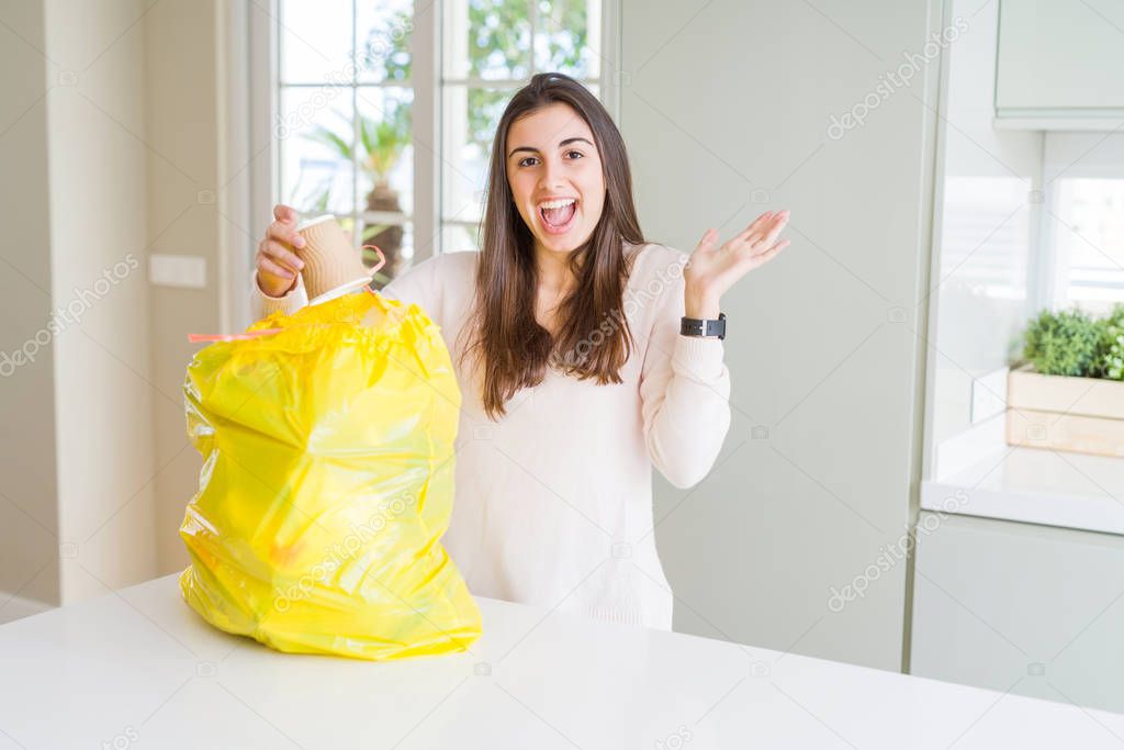 Beautiful young woman taking out the garbage from the rubbish container very happy and excited, winner expression celebrating victory screaming with big smile and raised hands