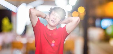 Genç yakışıklı adam izole arka plan üzerinde kırmızı t-shirt giyen rahatlatıcı ve kollar ve eller baş ve boyun arkasında germe, mutlu gülümseyen