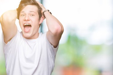 T-shirt üzerinde arka plan deli izole ve ile korkuttu casual beyaz giyen genç yakışıklı adam kafasına, korkmuş ve şaşırmış şok açık ağız ile eller