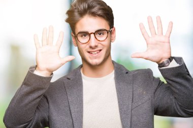 Genç iş adamı izole arka plan üzerinde gözlük giyiyor ve parmak numarası on ile işaret kadar emin ve mutlu gülümseyen.