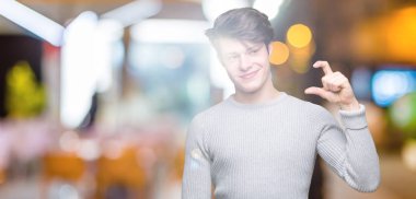 Yakışıklı genç gülümseyen izole arka plan ve boyutu işaret parmaklı ararken ve kamera işi el ile kendinden emin eller üzerinde kış kazak giyiyor. Ölçü kavramı.