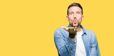 Bir öpücük el ile güzel ve seksi olmak hava üfleme kamera bakarak denim ceket giyen sakal ve mavi gözlü yakışıklı adam. Aşk ifade.