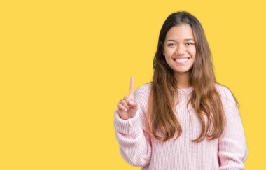 Ve parmak gülümseyen süre bir numara ile kendinden emin ve mutlu yukarıyı gösteren izole arka plan üzerinde pembe kış kazak giyen genç güzel esmer kadın.