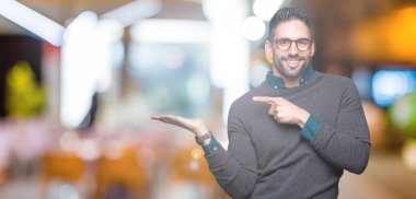 Hayret ve el ile sunulması ve parmak ile işaret ederken kameraya gülümseyen izole arka plan üzerinde gözlük takan genç yakışıklı adam.