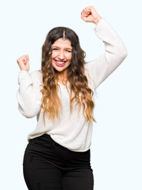 Beyaz kazak giyen genç güzel kadın çok mutlu ve heyecanlı kollarını kaldırdı ile kazanan jest yapıyor, gülümseyerek ve başarı için çığlık. Kutlama konsepti.