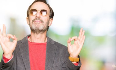 Orta yaş yakışıklı iş adamı giyen güneş gözlüğü rahatla ve gülümseyen gözlerle kapalı parmak jestle meditasyon yapıyor. Yoga kavramı.
