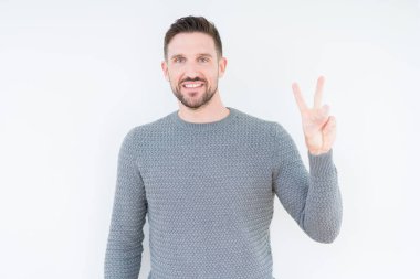 Genç yakışıklı adam izole arka plan üzerinde rahat kazak giyiyor ve parmaklar iki numarası ile işaret kadar emin ve mutlu gülümseyen.