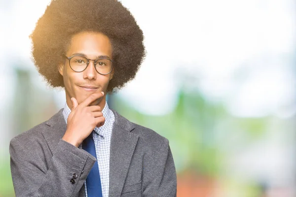 Young african american business man with afro hair wearing glasses looking confident at the camera with smile with crossed arms and hand raised on chin. Thinking positive.