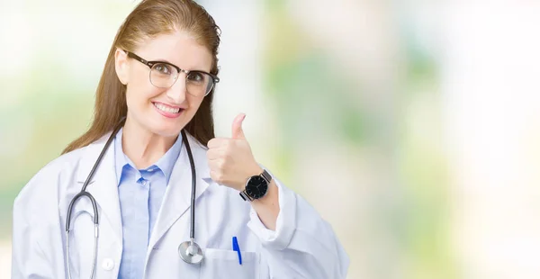 中年成熟的医生妇女穿着医疗外套在孤立的背景做快乐的大拇指用手的手势 查看显示成功的相机的审批表情 — 图库照片
