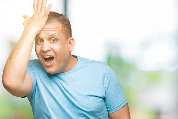 Middle age arab man wearing blue t-shirt over isolated background surprised with hand on head for mistake, remember error. Forgot, bad memory concept.